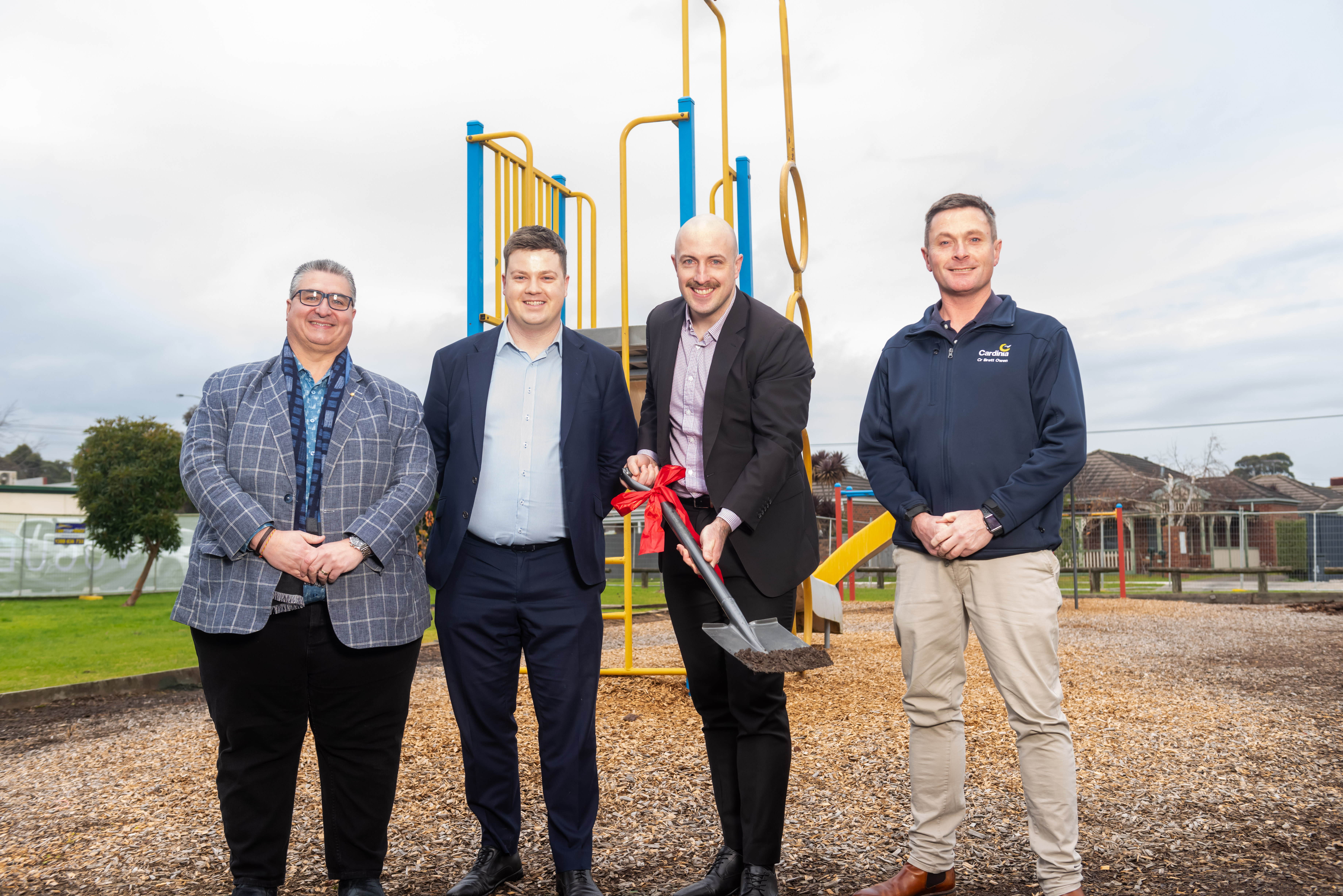 Four men stand in front of playground with a shovel with a red bow marking the first sod turn.