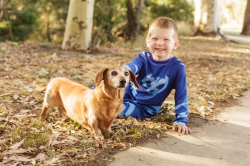 A small boy and his dog sitting beside a walking trail