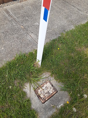 A fire hydrant port and marker post on a nature strip.
