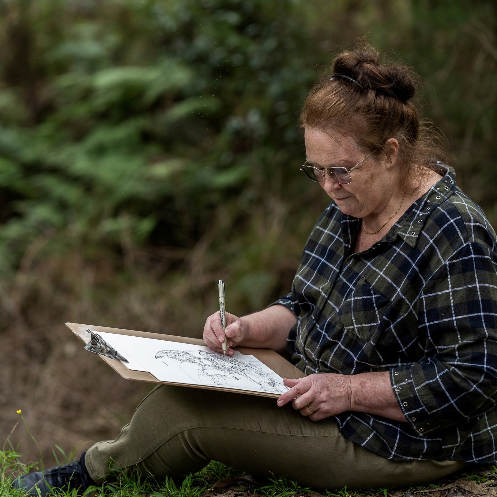 Photograph of Cardinia Shire artist, Jenni Ivins, sitting outdoors sketching on a large sheet of paper.