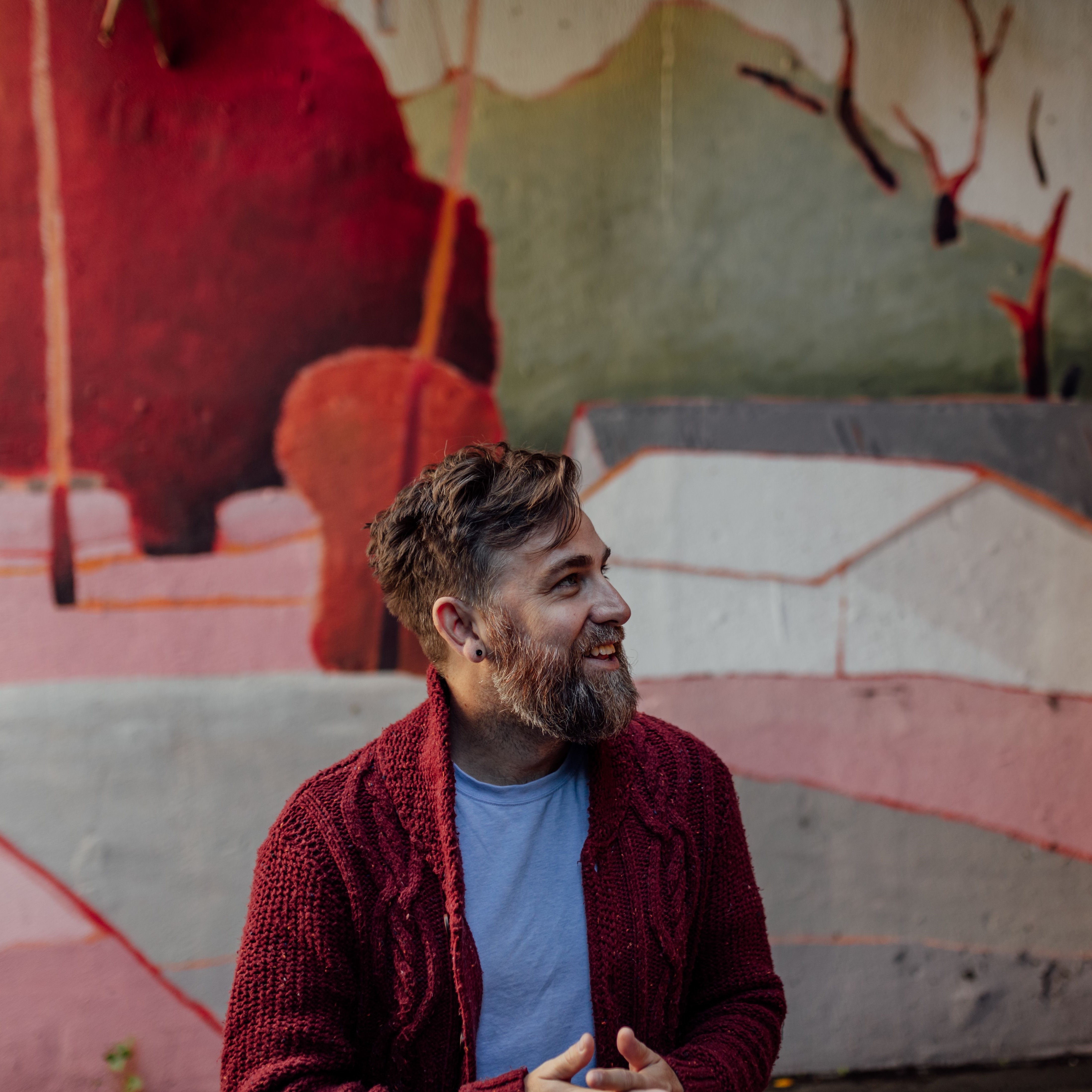 Josh Pyke sitting in front of a colourful wall looking sideways