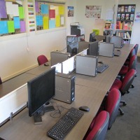 Long table with computers and keyboards, surrounded by desk chairs